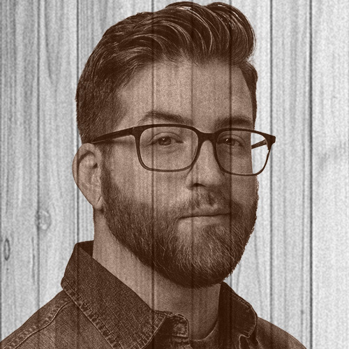 Dark-haired man with beard and glasses facing camera, transparent on wooden background